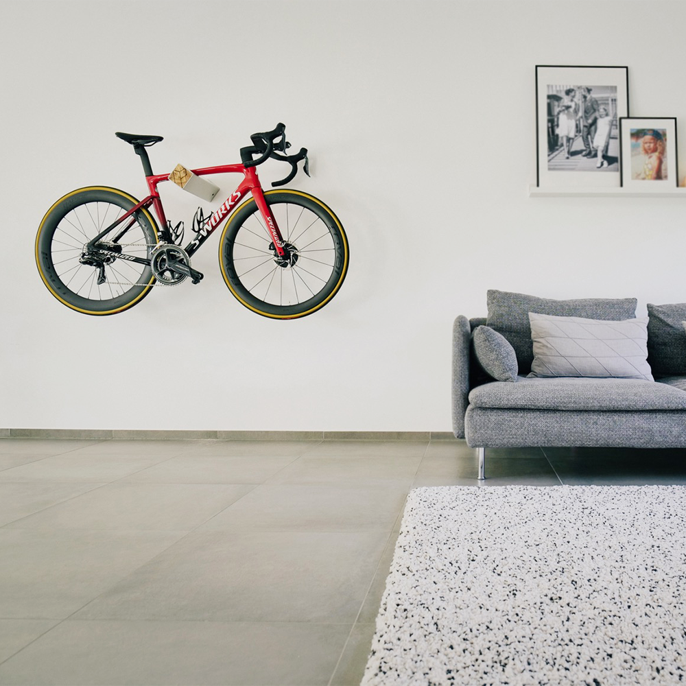 Silberne Fahrrad Wandhalterung D-RACK mit Olivenholzfront und rotem Fahrrad neben grauem Sofa mit Kissen vor weißer Wand