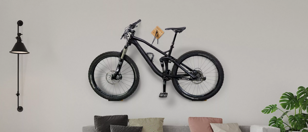 Schwarzes Fahrrad wird gehalten von Wandhalterung aus Holz vor grauer Wand und über Sofa mit bunten Sofakissen